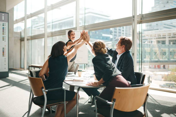 Shot of a group of businesspeople high fiving while sitting in a meeting